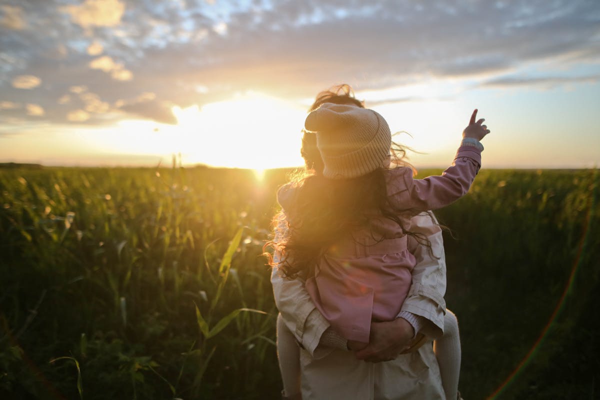 A parent holding their child, looking toward the sunset — protecting future generations from uncontrolled AI